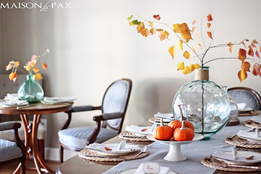 Lovely, simple Thanksgiving tablescape: a grand table and a side table with fall foliage centerpieces, simple neutral china settings, and a few pumpkins | maisondepax.com